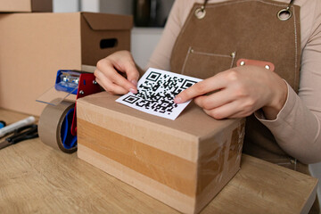 Woman affixing QR code onto packed cardboard box parcel. Concept organization, delivery service and technology in storage management.