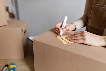 Young woman small business owner writing down word donation on box, preparing parcel for shipping...