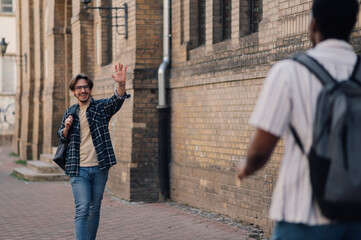 Two male students greeting each other waving in the street