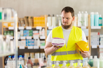Male builder in yellow vest with helmet in his hands chooses feminine pads in a supermarket