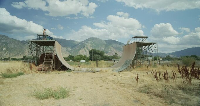 Man standing on top of ramp with blue wheelbarrow - wide, tracking shot