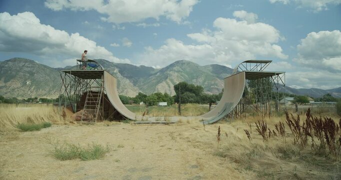 Slow motion dolly in on skating ramp with man on top with wheelbarrow