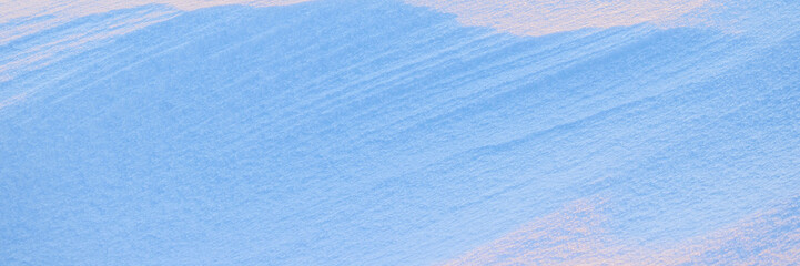 Beautiful winter background with snowy ground. Natural snow texture. Wind sculpted patterns on snow surface. Wide panoramic texture for background and design. Closeup top view with copy space.