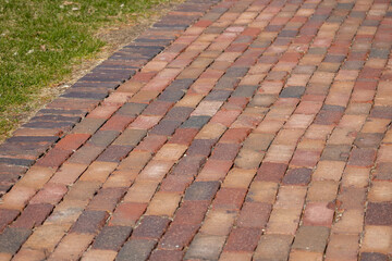 Fototapeta premium Full frame texture background of a colorful vintage red hued brick cobblestone pedestrian walkway in dappled sunlight