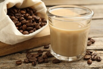 Coffee cream liqueur in glass and beans on wooden table, closeup