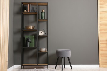 Shelving unit with decor, stool and folding screen near grey wall indoors