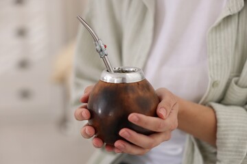 Woman drinking traditional yerba mate tea indoors, closeup