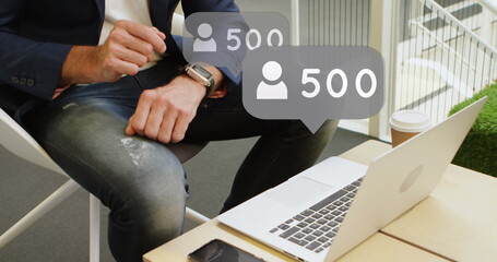 Image of emoji icons and numbers over man using smartwatch and laptop