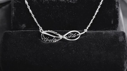 Delicate silver infinity pendant necklace with customized inscriptions displayed on dark velvet display case