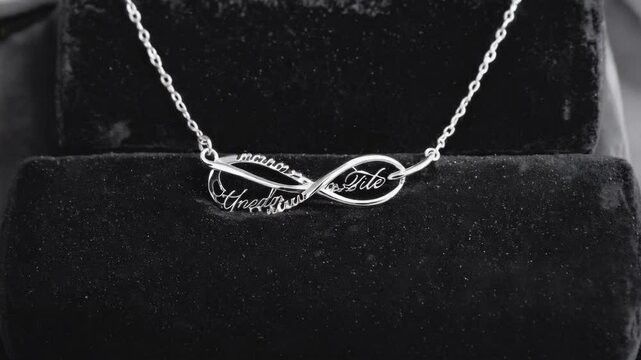 Delicate silver infinity pendant necklace with customized inscriptions displayed on dark velvet display case