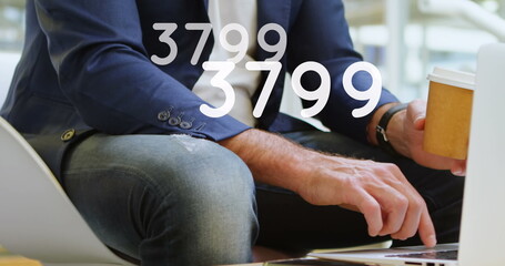 Image of growing numbers over man using laptop