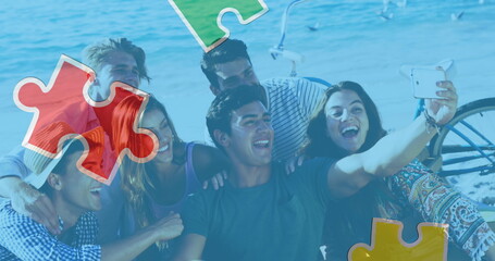 Image of colourful puzzle pieces over happy friends at summer beach party