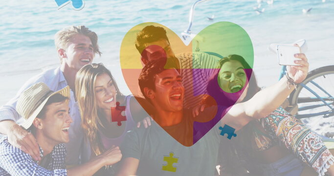 Image of colourful puzzle pieces heart over happy friends at summer beach party
