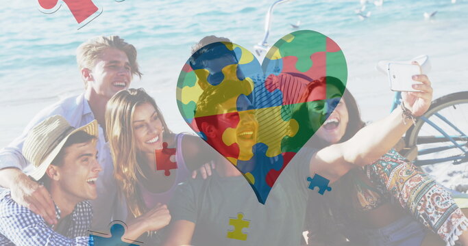 Image of colourful puzzle pieces heart and autism text over happy friends at summer beach party