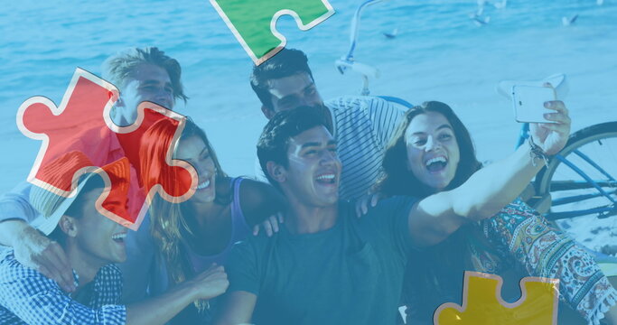 Image of colourful puzzle pieces over happy friends at summer beach party