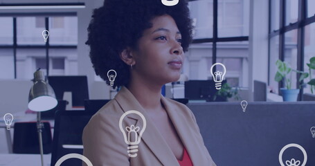 Image of lightbulb icons over african american businesswoman thinking in office