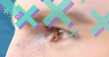 Image of cross icons over eye of caucasian man on blue background