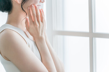 窓際でお肌を触る女性（美容・スキンケア・基礎化粧品イメージ）
