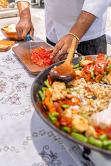 Chef chopping tomatoes while preparing paella outdoors