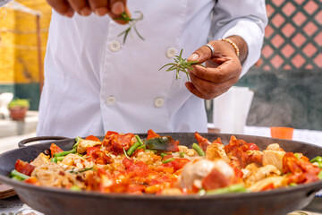 Chef adding rosemary to delicious paella outdoors