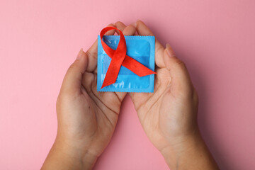 Red Awareness Ribbon On Condom Lying On Palm Hands Isolated On Pink Background