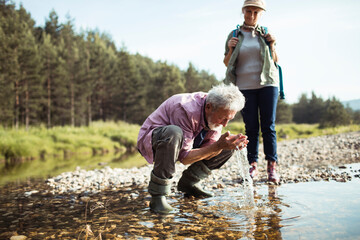 Senior man drinking water from river during hiking trip