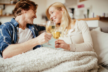 Mid adult couple enjoying a glass of wine while sitting in the living room under a blanket