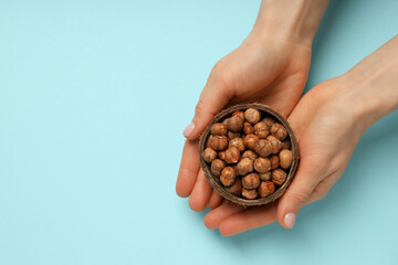 Peeled hazelnuts in coconut shell in female hands on blue background, space for text