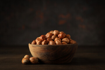Bowl with peeled hazelnuts on wooden table on dark background, close up