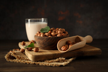 Hazelnuts in bowl, glass of milk and scoop on wooden board on dark background, close up