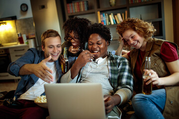 Young and diverse group of friends watching a movie on laptop in the living room on the couch
