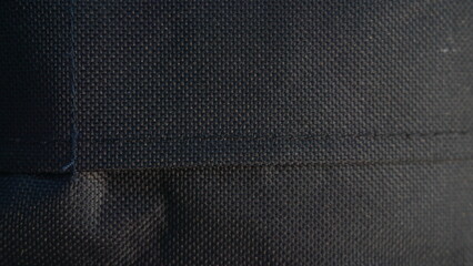 Close-up dark fabric seam, outdoor sunlight, background blurred