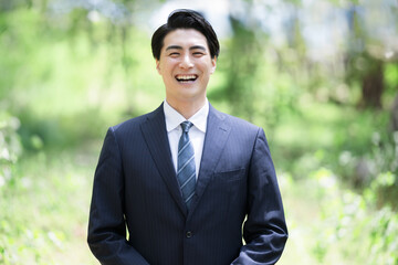新緑背景でスーツを着た男性のカメラ目線の笑顔