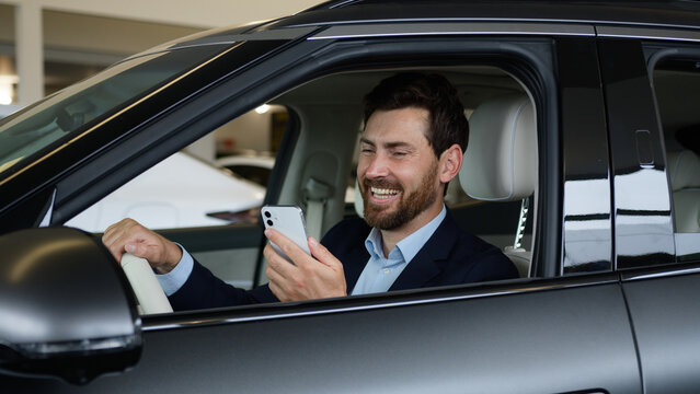 Caucasian man businessman new car automobile auto owner user mobile phone smartphone internet social networks humor laugh male smiling funny business guy inside adult salon dealership transport buying