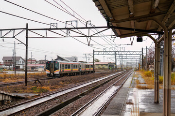 Fototapeta premium JR上越線のローカル電車が入ってきた。 JR五日町駅。 寂れた雰囲気が良い感じ。 五日町の市街地の風景。 雪国特有の雰囲気がある。 晩秋なので各所で紅葉が見られる。 新潟県魚沼市 - 2024年11月30日 