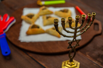 Sweet triangular gomentashi ears of aman for the holiday of Purim on the table in the foreground a rattle