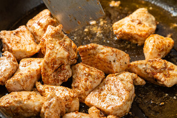 Chicken fillet pieces are fried in a frying pan in sauce and spices and turned over