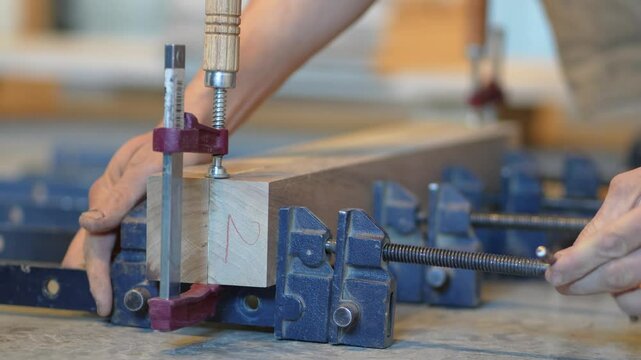 Experienced woodworker hands adjusting clamps, ensuring firm adhesion and seamless wood joining with steel mechanism. Expert carpentry, joiner craftsmanship, wood stability, precise bar alignment