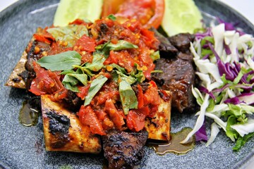 Indonesian grilled beef ribs smashed and served with spicy sambal. Iga Bakar Penyet is a flavorful traditional dish, often enjoyed with rice and fresh vegetables.