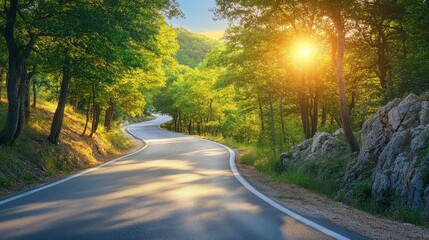 Fototapeta premium Scenic winding road through lush forest at sunset. Sunlight streams through trees casting shadows on the asphalt
