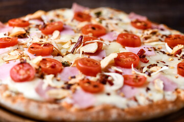 Pizza with ham, cherry tomatoes and mozzarella cheese. Wooden background. Soft focus. Close up.	