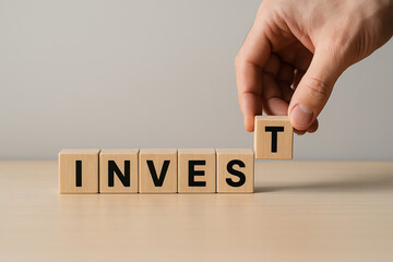 A hand rearranging wooden blocks to spell the word 'INVEST', symbolizing financial growth and investment. Captivating imagery to illustrate the concepts of finance and planning.