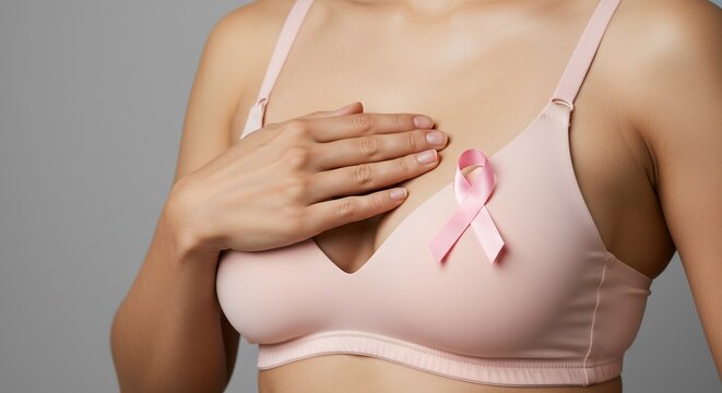 Woman's hand gently touching her breast with a pink ribbon, breast cancer awareness concept