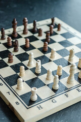 A wooden chessboard with light and dark pieces arranged mid-game, placed on a dark surface. The shot captures strategic tension with a slightly tilted top-down perspective © Daniel