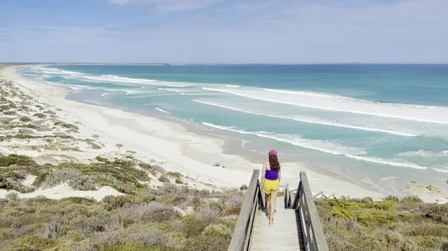 girl stands on wooden stairs with platform and looks at rock pools and Daly Head beach with turquoise water and powerful waves. Thidna Conservation Park, Yorke Peninsula, Adelaide, South Australia