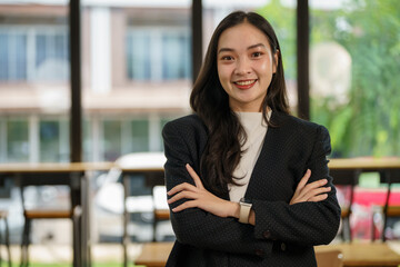 Professional Asian businesswoman confidently standing with crossed arms in the contemporary workplace, embodying corporate success.