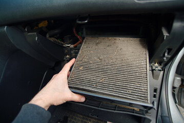 Closeup of person removing dirty cabin air filter from car during regular maintenance showing dust buildup and the importance of clean air in vehicle interiors. Selective focus