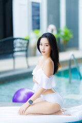 Charming Asian woman sitting on pool float in white bikini outfit
