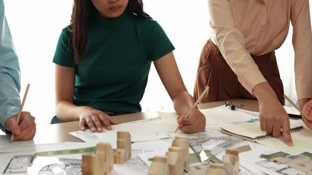 Smart architect and safety engineer discussion about building blueprint on table with architectural document, measurement tools and wooden block scatter around at modern office. Closeup. Delineation.