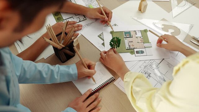 Architect and engineer use tree model discuss about building blueprint on table with architectural document, measurement tools and wooden block scatter around at modern office. Closeup. Delineation.